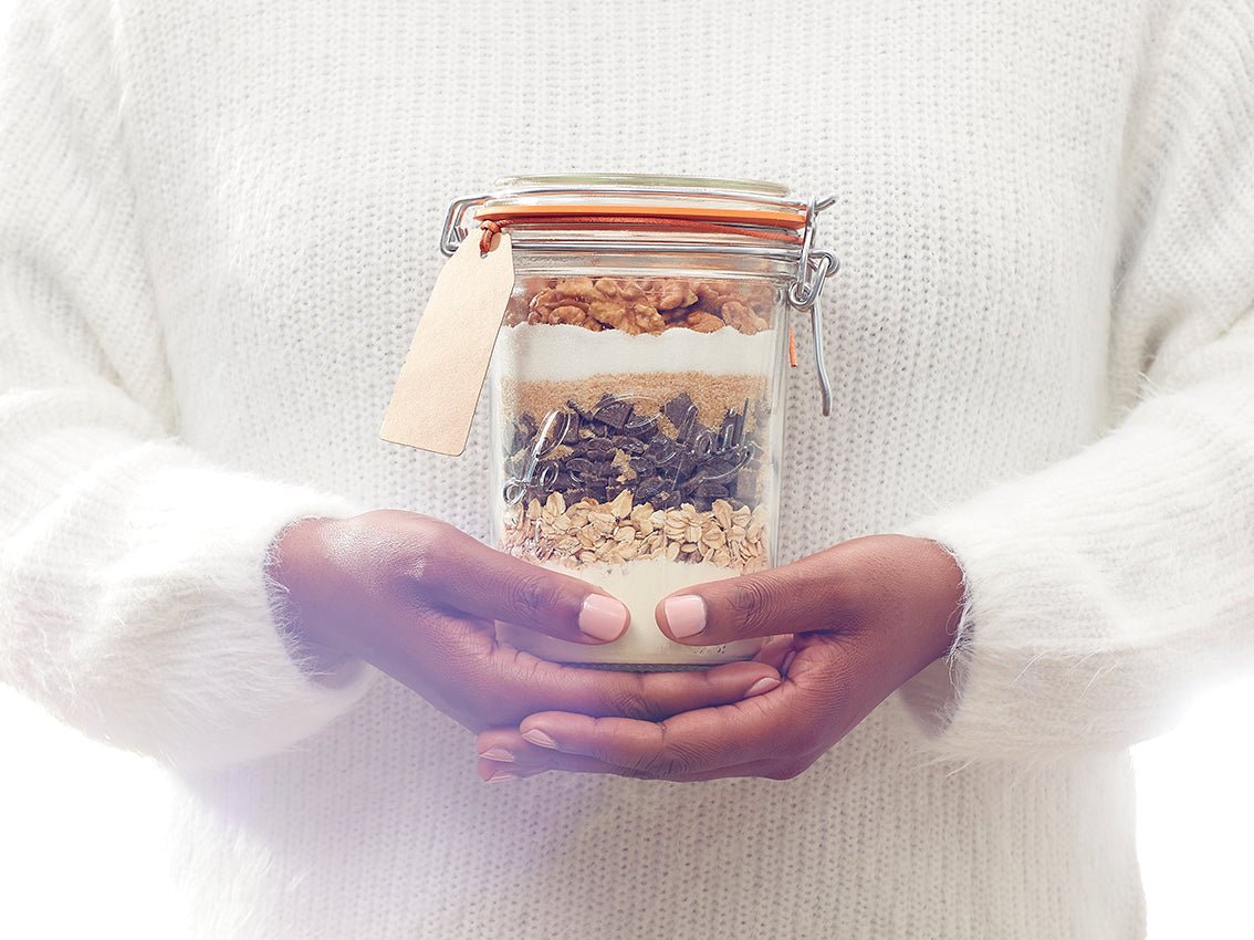 Hands holding a Le Parfait jar layered with cookie mix and tied with a gift tag