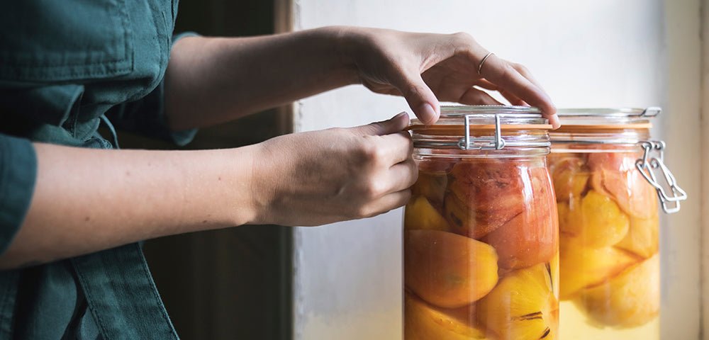 Hands sealing a Le Parfait Super Jar of home-canned tomatoes by a window