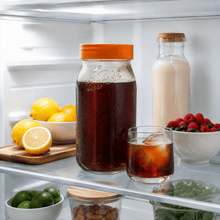 Load image into Gallery viewer, A clear glass Le Parfait Screw Top jar with orange lid filled with cold brew coffee, displayed on a refrigerator shelf alongside a glass of cold brew coffee, a bottle of milk, lemons, berries, limes, and nuts.
