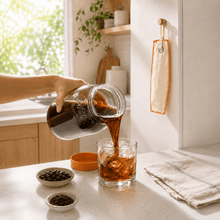 Load image into Gallery viewer, A hand pours freshly brewed dark cold brew coffee from a glass Le Parfait 2L Screw Top jar into a clear glass with ice on a kitchen counter, with small bowls of coffee beans and a folded cloth nearby.
