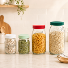 Load image into Gallery viewer, Four clear glass canisters with colorful lids in a kitchen setting, filled with beans, lentils, rotini pasta, and oats. The jars are embossed with the brand name 'La Felicia'.