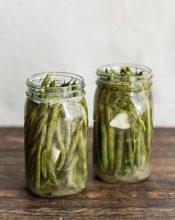 Load image into Gallery viewer, Two glass jars filled with fermented green beans on a wood table.