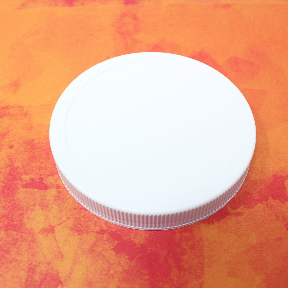 Single white plastic Le Parfait Familia Wiss screw-top lid, angled view on an orange watercolor background.