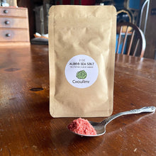 Load image into Gallery viewer, ChouAmi Alaea Sea Salt 2oz kraft pouch with a spoonful of red-hued sea salt on a wooden table.