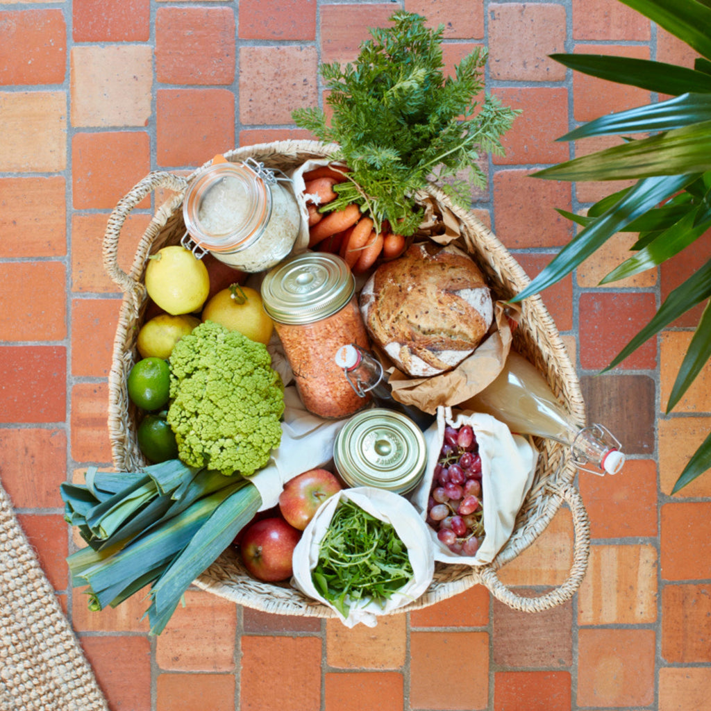 Top-down market basket with a Le Parfait Swing Top Bottle of juice among lemons, leeks, romanesco, apples, carrots, grapes, and fresh bread.