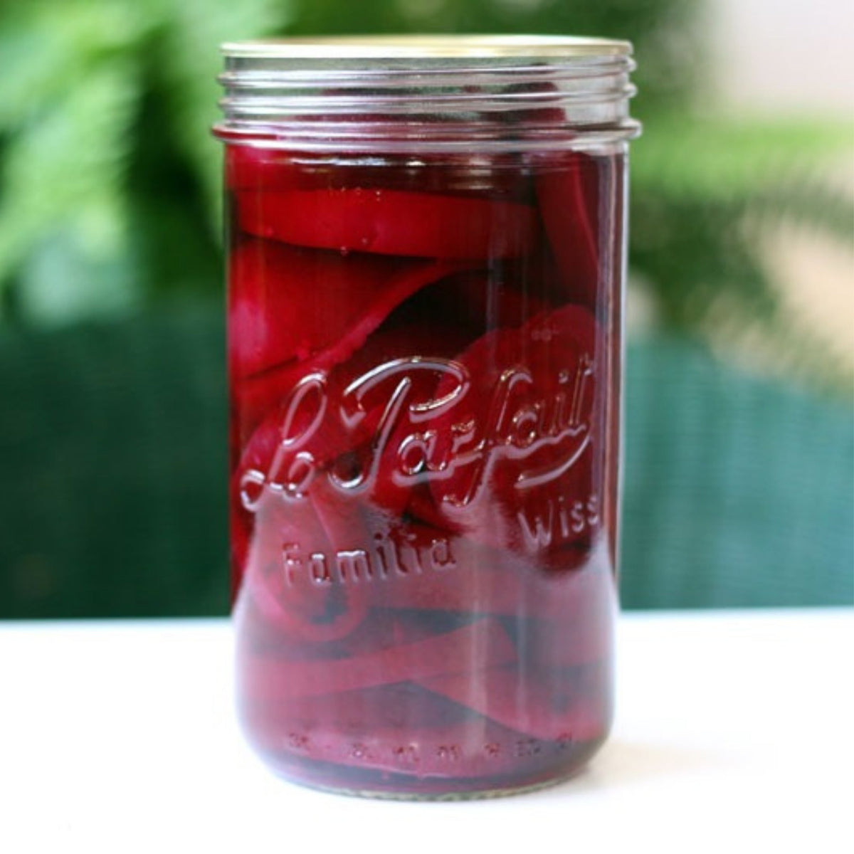 Le Parfait Familia Wiss terrine of pickled red beets and onions in vinegar brine on a green outdoor surface.