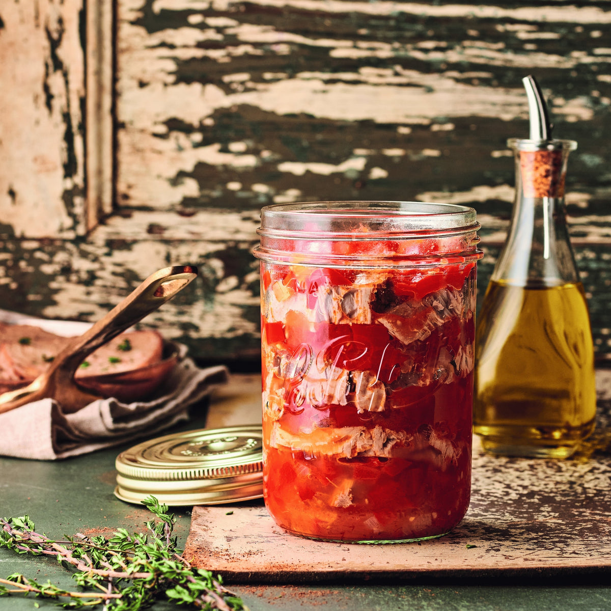 Open Le Parfait Familia Wiss terrine of tomato confit with thyme on a weathered green plank, beside an olive oil cruet.