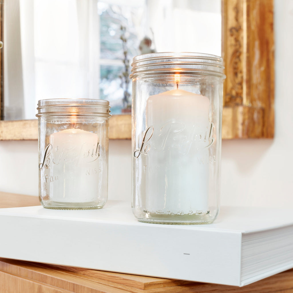 Two Le Parfait Familia Wiss terrines repurposed as candle holders with lit white pillar candles on a console table.