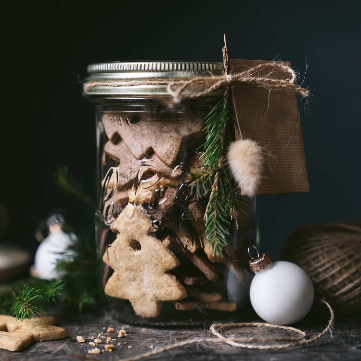 Le Parfait Familia Wiss terrine of star-shaped gingerbread cookies tied with twine and a kraft tag, beside Christmas ornaments and pine sprigs.