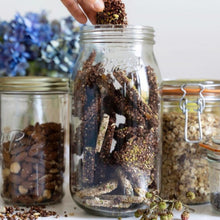 Load image into Gallery viewer, Hand reaching into an open Le Parfait Screw Top Jar of homemade seed-and-grain energy bars beside jars of almonds and granola, with blue hydrangea.