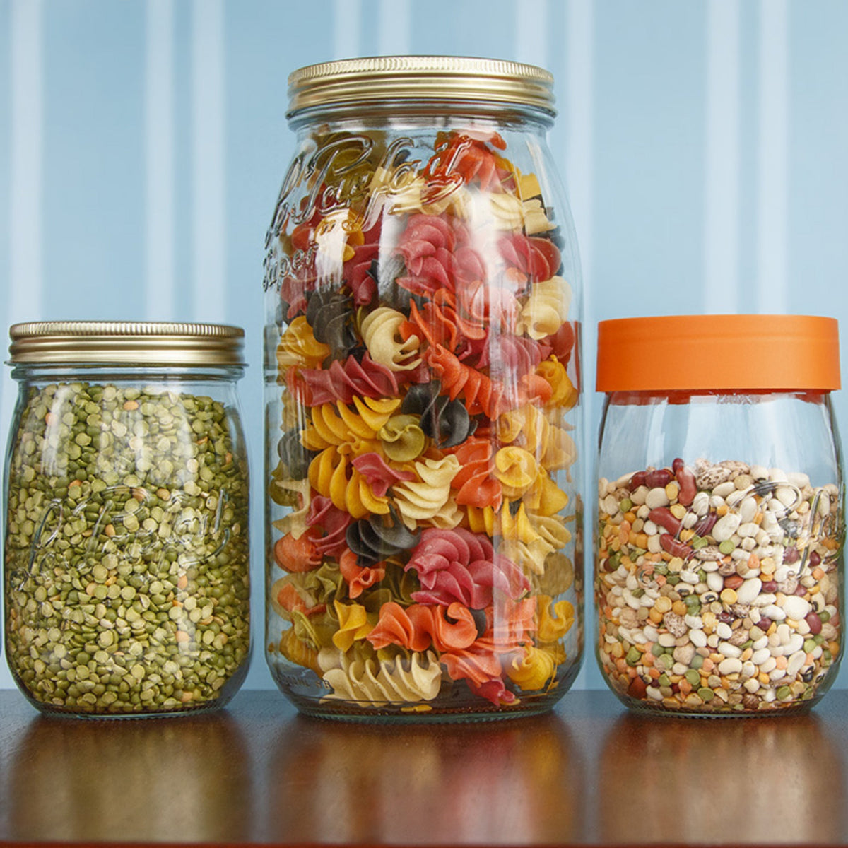 Le Parfait Screw Top Jars in a pantry display - gold metal-lid split peas, gold metal-lid multicolor pasta, and orange-lid mixed beans.