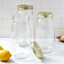 Load image into Gallery viewer, Three empty Le Parfait Super jars with gold metal canning lids on a white marble counter beside fresh lemons, one jar open with its lid alongside.