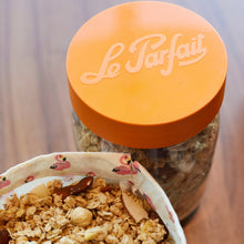 Load image into Gallery viewer, Close-up of an orange Le Parfait screw lid on a jar of homemade granola beside a flamingo-print fabric napkin holding more granola.