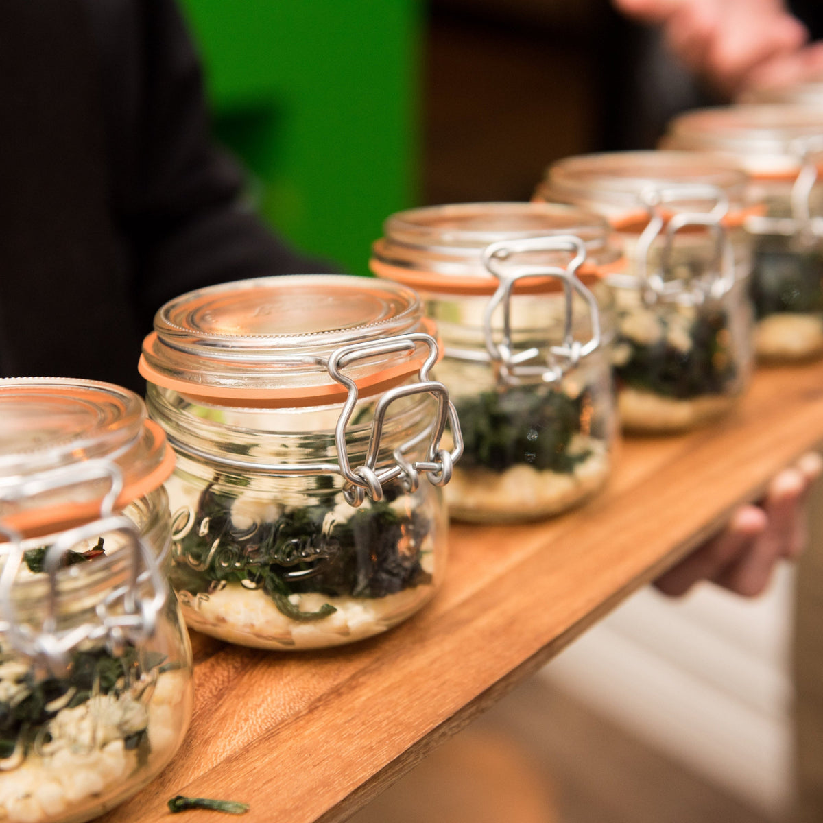 Row of Le Parfait Super Jars on a wooden bar, each filled with sauerkraut fermenting in a workshop setting.
