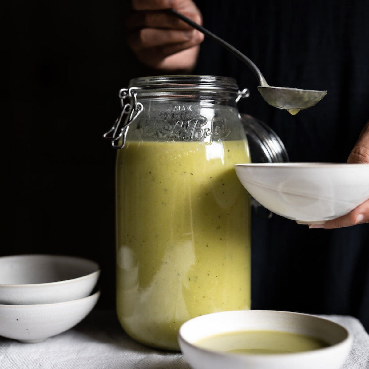 Large Le Parfait Super Jar of creamy green vegetable soup being ladled into ceramic bowls.
