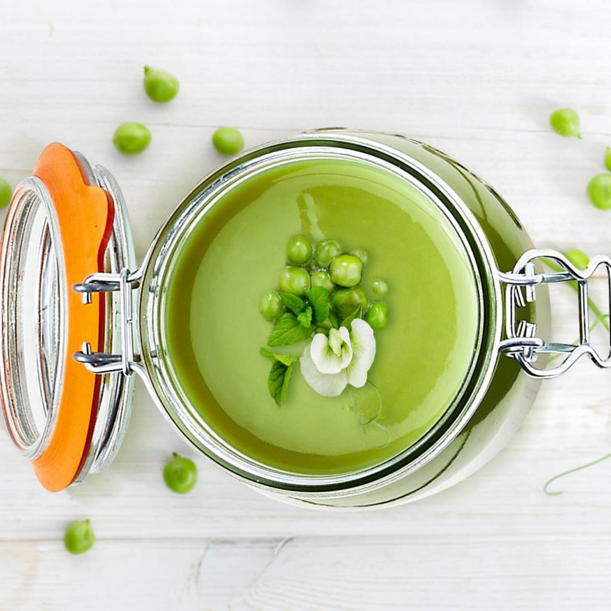 Top-down view of an open Le Parfait Super Jar filled with chilled pea soup, garnished with fresh peas, mint, and an edible flower.