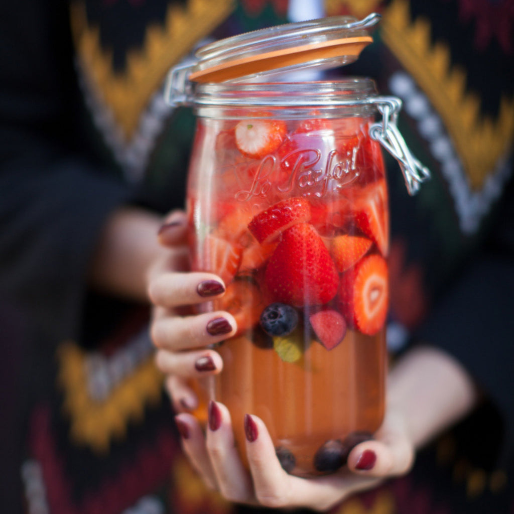 Hands holding a 2L Le Parfait Super Jar of strawberries and blueberries macerating in syrup.
