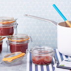 Le Parfait Super Terrines of apple compote on a striped tea towel with a saucepan and turquoise ladle in the background.