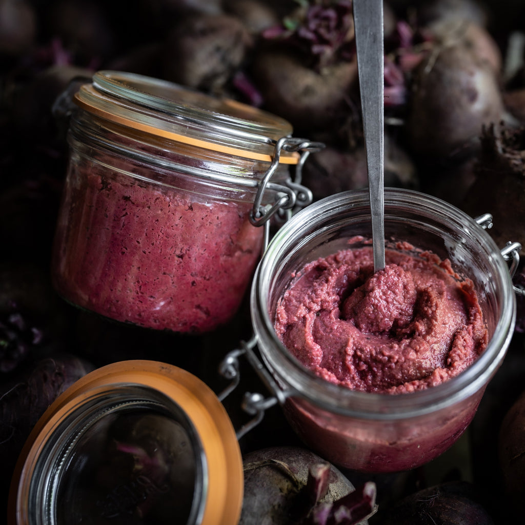 Two open Le Parfait Super Terrines of beet hummus served with a spoon on a bed of fresh red beets.