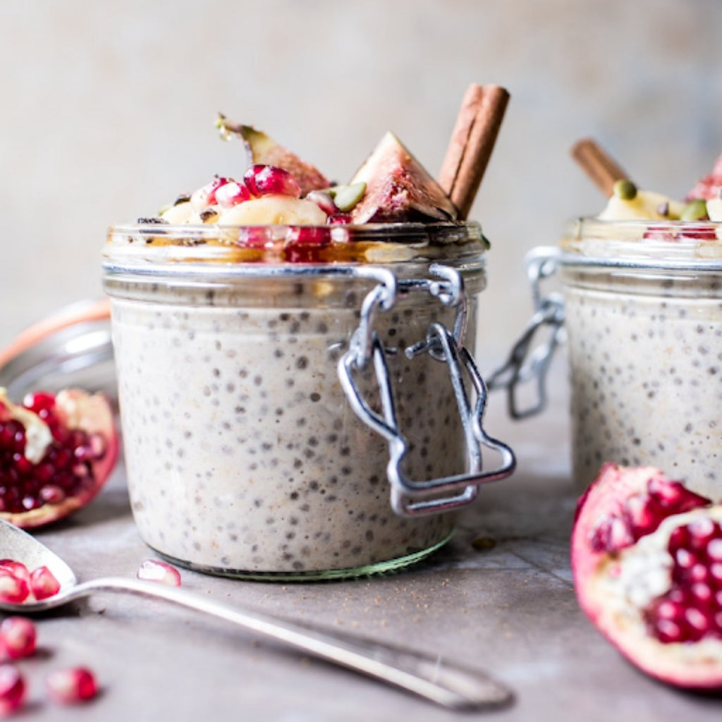 Two Le Parfait Super Terrines of chia pudding topped with fig, pomegranate seeds, and cinnamon sticks on a stone surface.