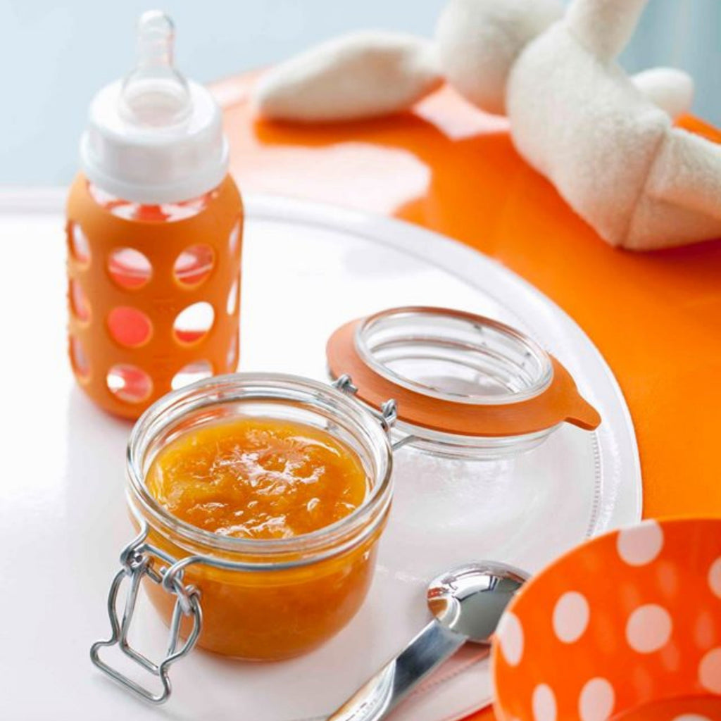 Le Parfait Super Terrine of homemade apricot puree beside a baby's bottle and plush rabbit on an orange tray.
