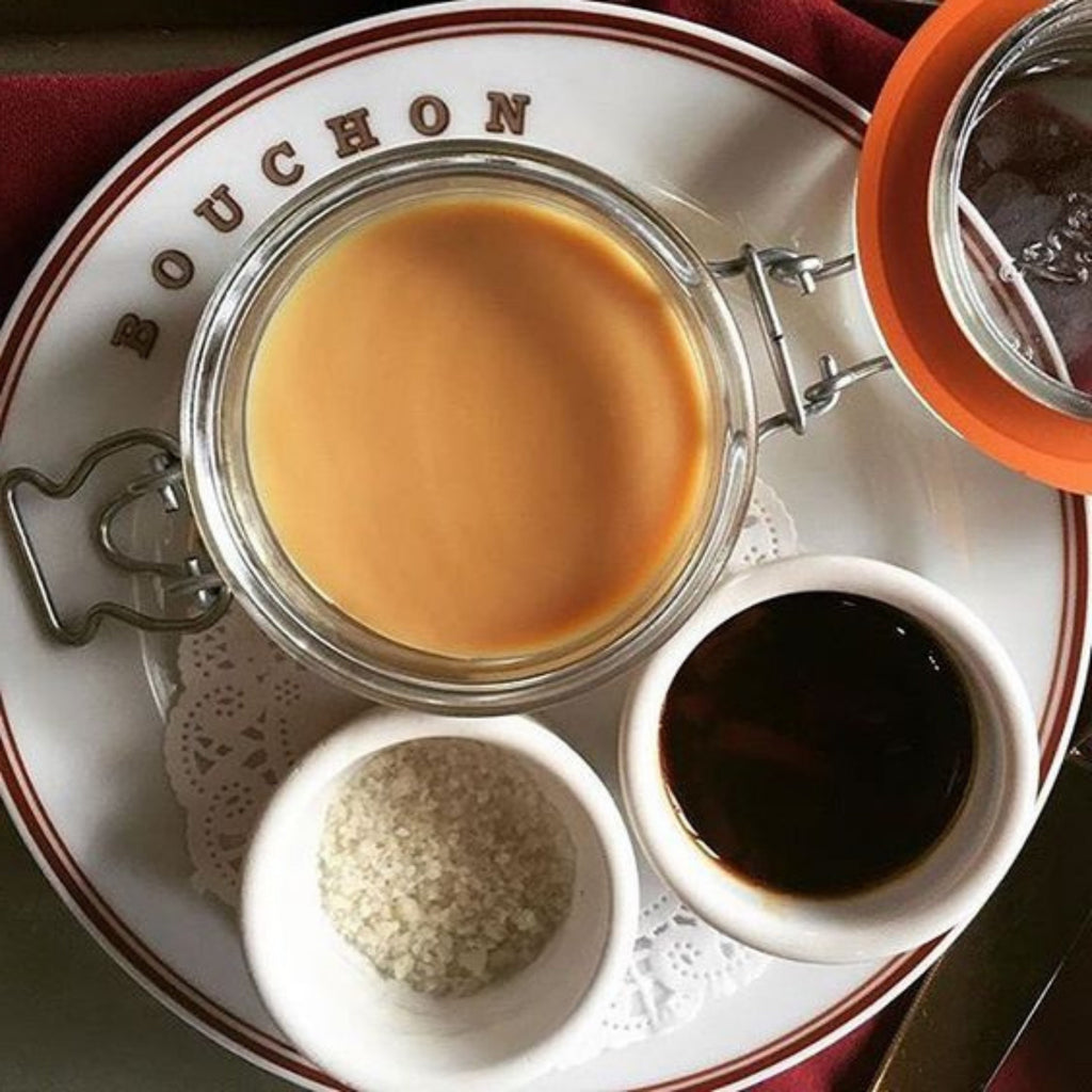 Top-down French bistro plating with a Le Parfait Super Terrine of crème caramel on a Bouchon-branded plate, accompanied by sugar and caramel syrup.