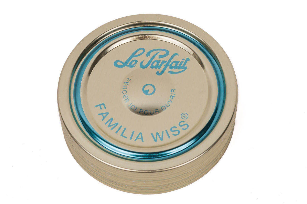Top-down Le Parfait Familia Wiss gold sealing cap with teal 'pierce-here' indicator and 'Le Parfait Familia Wiss' branding.
