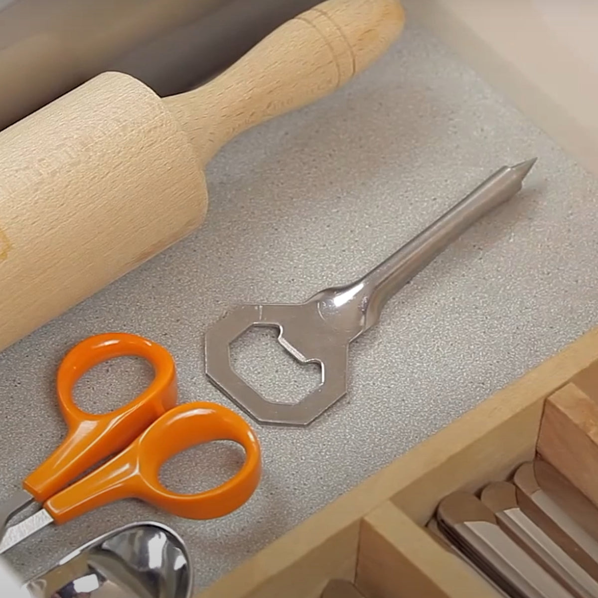 Le Parfait Tire-Rondelle opener resting in an open kitchen drawer beside a rolling pin, scissors, and other utensils.