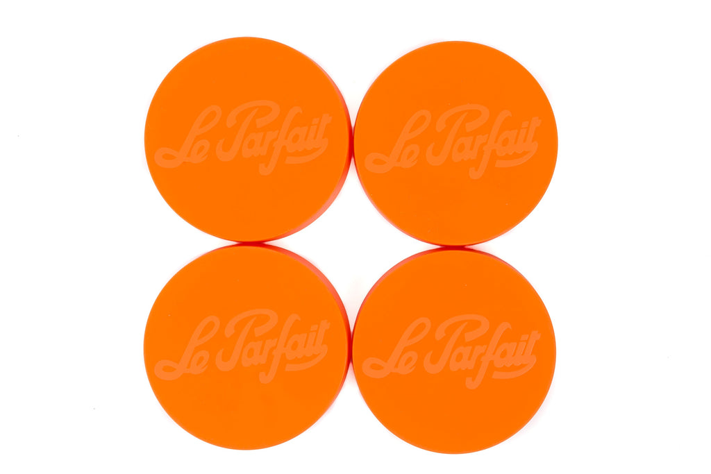 Four sparkling orange Le Parfait plastic screw-top jar lids with embossed logo, top-down view on white.