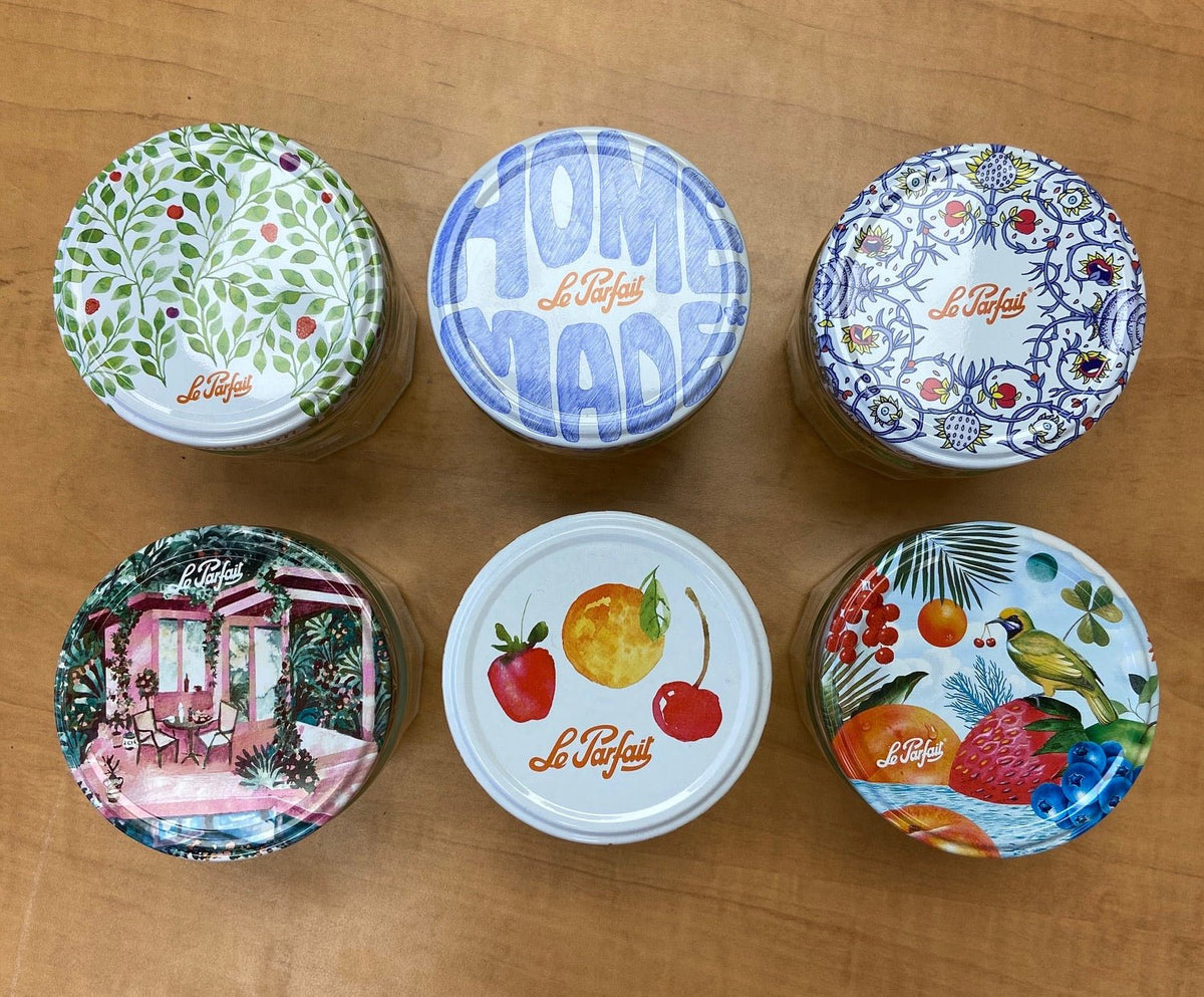 Le Parfait 82mm Twist Lid sampler - six designs: botanical, Homemade, Provençal, garden cabana, watercolor fruit, and tropical pattern, on wood.